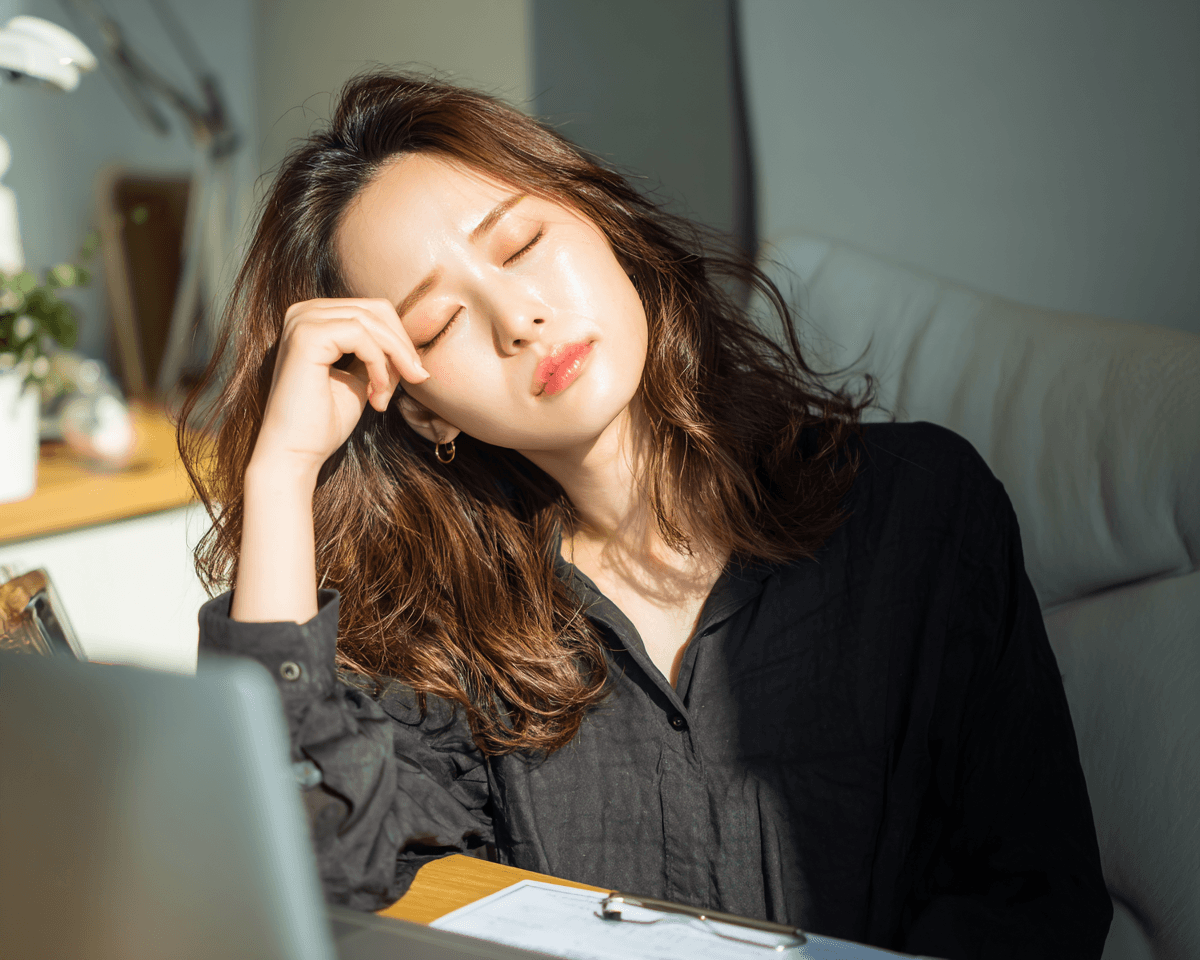 햇빛이 들어오는 사무실에서 눈을 감고 피곤한 표정을 짓고 있는 여성